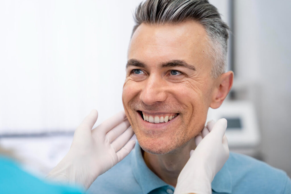 Homem sorridente com cabelos grisalhos e dentes alinhados durante avaliação para implante dentário na Clínica R7 Implantes no Catete, RJ.