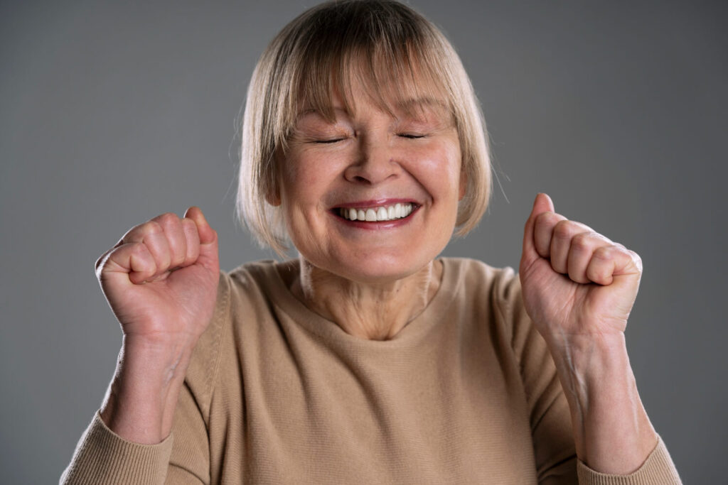 Mulher idosa comemorando com sorriso fixo de prótese protocolo no Catete, destacando o fim do céu da boca coberto.