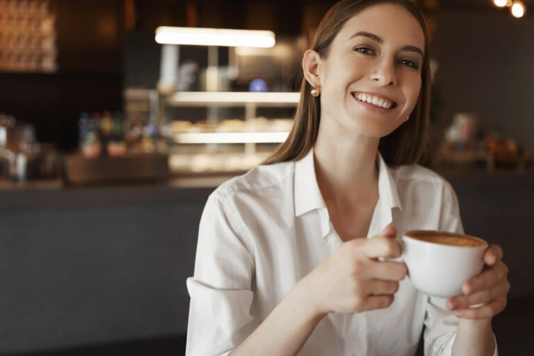 Mulher sorridente segura xícara de café, ilustrando a resistência de facetas em resina na Clínica R7 Implantes, no Catete RJ.