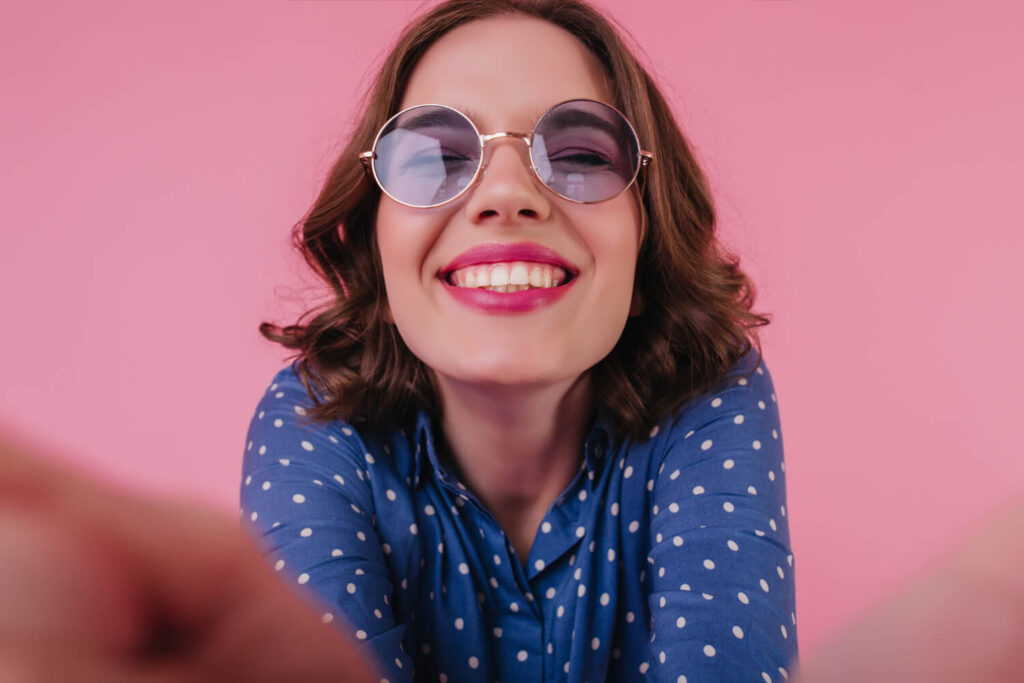 Mulher jovem de óculos escuros sorrindo com dentes brancos alinhados após lentes de contato dental na Clínica R7 no Catete, Rio de Janeiro.