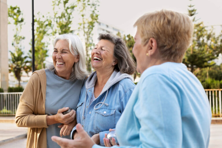 Três amigas seniores rindo ao ar livre. Na R7 Implantes no Catete - RJ, o metal do implante dentário não fica visível no sorriso.